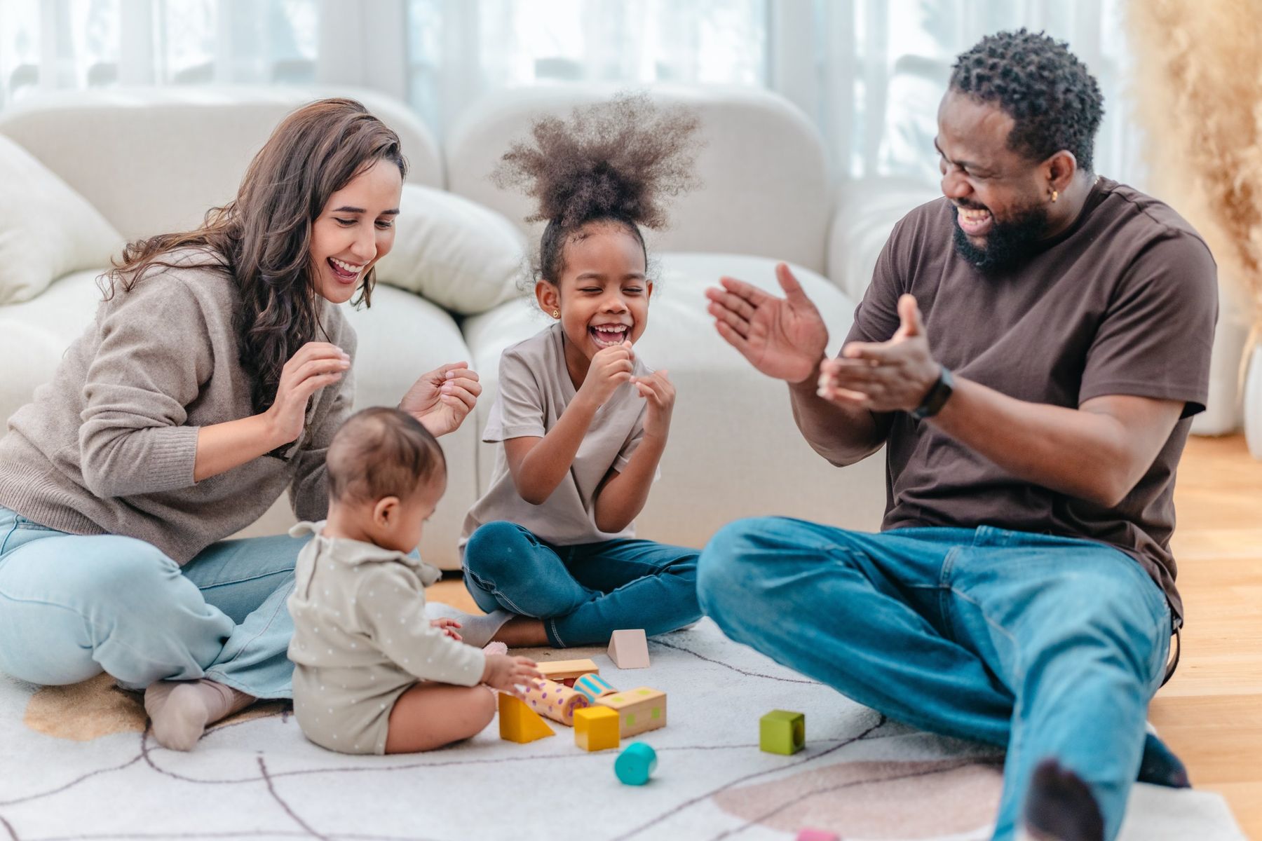 Parents laughing and playing with their two young children on the floor