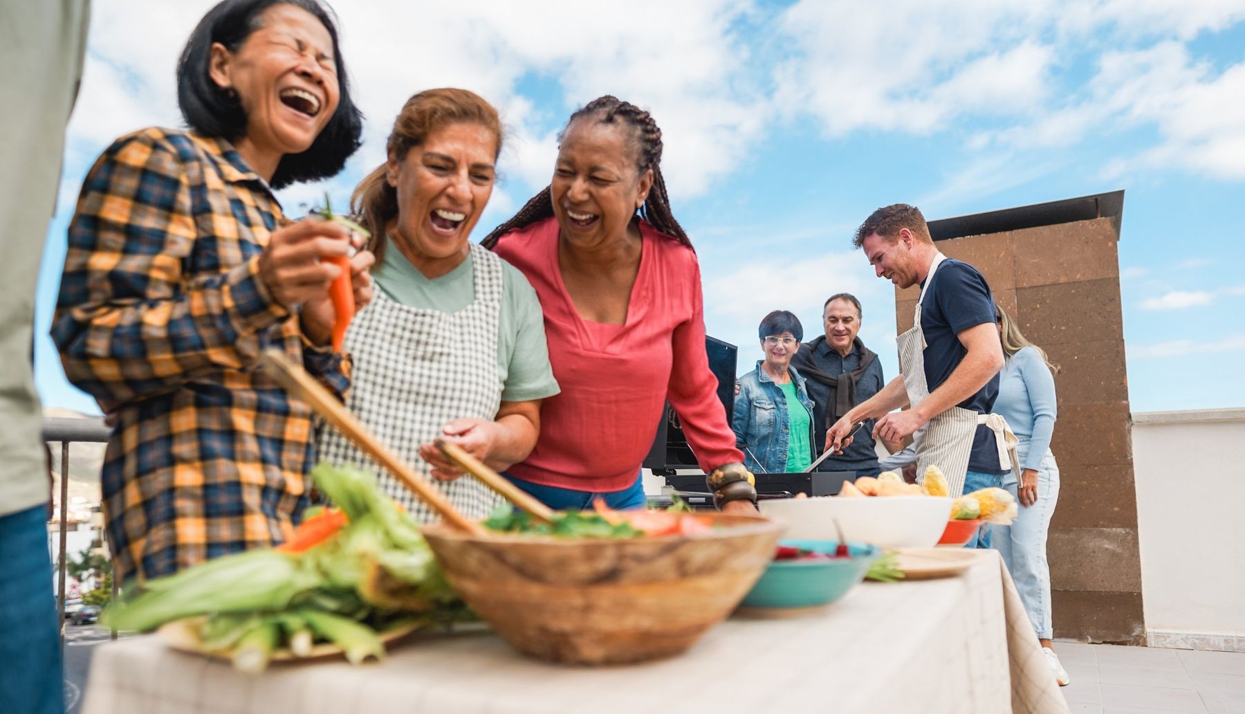 Older women laughing together while cooking outdoors